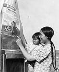 Inuit woman and child looking at a Family Allowances poster, Baker Lake (Qamanittuaq), Northwest Territories [Nunavut], 1948 [The woman has been identified as Winnie Attungala.] 1948.