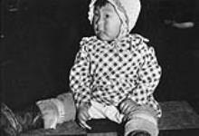 Unidentified Inuit infant wearing a bonnet and dress with a chequered print ca. 1955.
