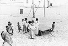 Inuit woman and children loading an elderly Inuit man, who is unable to walk, onto a cart [graphic material] 1965