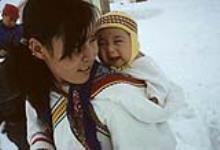 Young mother and her baby: the mother is wearing an amauti and her baby is wearing a yellow hat. [Damaris Ittukusuk Kadlutsiak was the first wife of Josiah Kadlutsiak of Igloolik. She is packing her son, Mike Kadlutsiak] [graphic material] May 1965.
