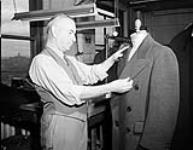 Tailor adjusting a suit jacket that is hanging from a dummy 12 Sept. 1946