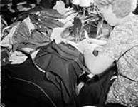Woman sewing, the machine surrounded by piles of garments 12 Sept. 1946