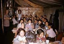 Groupe d'élèves en train de manger dans la tente-cafétéria, et membres du personnel de l'école, École (foyer-tente) de Coppermine (Kugluktuk) (Nunavut), [1958] 1958 ?.