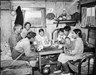 [Inuit family gathers in the home of Jimmy Gibbons. Left to right: Nakasuk Twotoongie, Joe Gibbons, Nellie Gibbons, ?, Mike Gibbons, Jimmy Gibbons, Caroline Gibbons holding Nuati Gibbons. Location is Arviat, Nunavut] Jimmy Gibbons, Inuit deputy RCMP constable at home with his family at Eskimo Point, N.W.T [graphic material] August 1, 1946