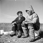 Two unidentified Inuit men [man on left is John Kugak] sitting on rocks talking to each other [graphic material] August 1, 1946