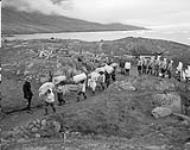 Inuits portant des sacs de courrier, livrés par le C.D. Howe, au bureau de poste à Pangnirtung juillet 1951.