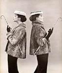 Two models, back to back, dressed similarly in fur coats and wearing hats, holding cane handled umbrellas n.d.
