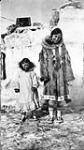 Inuit woman and child in front of a structure [The woman is Susie Sydney (née Carpenter). The young girl is Agnes Carpenter, whom Susie raised, is the daughter of the late Fred Carpenter. Susie and Fred were siblings.] 1931.