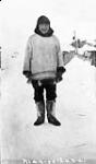 Inuk man "Mangelana" standing in the snow in front of building 1909