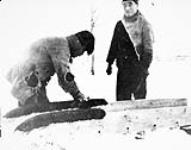 Uluksak and Sinisiak mudding up the qamutiik (sled) runners 1919