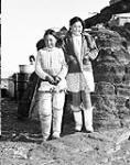 Two Inuit girls standing in front of a building n.d.