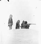 Inuk man using a rifle with three individuals behind him 1950
