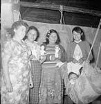 [Pukatawagan Indian Reserve, Manitoba - A group of women gather around an infant in a baby swing] [ca. 1960].