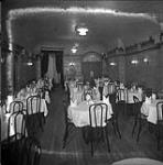 Interior view of a dining hall, empty, with tables set for dining ca 1930s.