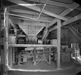 Interior view of an unidentified factory, showing stacks of newspapers on a shelf ca 1930s.