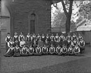 Group portrait of young women, possibly a school group. Young women are wearing insignia on the front of their dresses 1939.