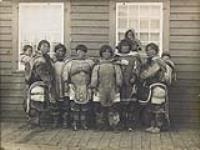 Inuit women and children in front of a frame building at Kuujjuarapik, (formerly Great Whale River), Quebec [graphic material] [between 1901-1904].
