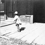 [Child walking on wooden sidewalk in front of stores] 1897.