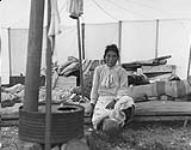 An Inuit woman sitting inside of a tent that has a stove, in Kangiqsujuaq (formerly Wakeham Bay), Quebec 1948.