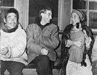 Sam Ford sitting with an Inuit man and woman holding a baby in Kangiqsujuaq (formerly Wakeham Bay), Quebec 1948.