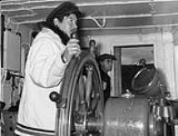 The Inuit pilot of the Eastern Arctic Patrol ship M.V. Regina Polaris, taking the ship up the Koksoak River to Kuujjuaq (formerly Fort Chimo), Quebec, with Sam Ford in the background 1948.