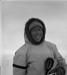 Inuit man in white parka and fur mittens, smiling January, 1946.