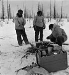 Two Inuit men and R.C.M.P. Corporal Jim Davies cooking food over a fire January, 1946.