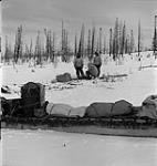 Two Inuit men and R.C.M.P. Corporal Jim Davies preparing food over a fire during their trip from Moose Factory Island, Ontario, to Whale River [Kuujjuarapik], Quebec January, 1946.