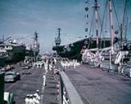 HMS ARK ROYAL and USS SARATOGA (at left and right) at Norfolk, Virginia pier with HMCS STADACONA band, International Naval Review, and Spanish naval training schooner JUAN SEBASTIAN de ELCANO in the foreground 10-Jun-57