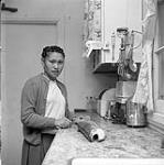 [Young woman [Elisappe Avinga] preparing a fish in a kitchen, Iqaluit, Nunavut] [between 1956-1960]
