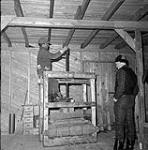 [Man operating a fur press while Red Pedersen observes, Kinngait, Nunavut] [between 1956-1960]