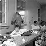 [Two people sewing while watching an infant indoors , Iqaluit, Nunavut] 1960