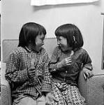 [Two children with lollipops sitting and smiling at each other, Iqaluit, Nunavut] 1960