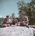 Un groupe de pêcheurs de deux hommes et d'une femme font une pause pour manger dans la région du Lac des Bois en Ontario July 1950