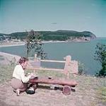 Artist Miss Billy Kinnear from Moncton, New Brunswick, paints Cape Owls Head from a shorepoint in Fundy National Park. In the background is the village of Alma, New Brunswick juillet 1950