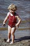 Une petite fille en maillot de bain rouge sur la plage, au parc national du Mont-Riding, au Manitoba juillet 1950
