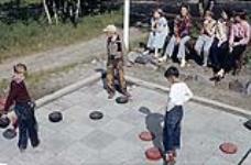 Three young boys play a giant game of outdoor checkers at Riding Mountain National Park, Manitoba juillet 1950