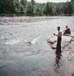 Two male tourists fish from the rocks on the shore of Lac Tremblant, Laurentian Mountains, P.Q.  1951