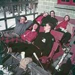 Deux hommes et quatre femmes prennent le soleil devant un chalet au centre de ski Camp Fortune sur les collines de la Gatineau au Québec mars 1952