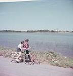 Man and woman on bicycles beside water, Prince Edward Island National Park  July 1953