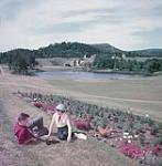 Man and woman seated on grass beside a flower bed, Fundy National Park, New Brunswick July 1953