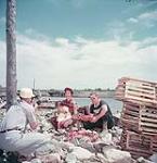 Man, woman and small child have their photo taken next to lobster traps, Fundy National Park, New Brunswick July 1953