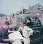 Deux hommes appuyés sur un fourgon consultent une carte, à Niagara July 1954