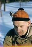 Gros plan d'un homme avec un oiseau posé sur sa tête (chapeau orange). Chalet Shilly Shally, parc de la Gatineau s.d.