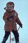 Gros plan d'un jeune skieur vêtu d'un manteau rouge et de lunettes orange. Mini-ski (probablement Camp Fortune) février 1964