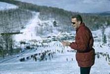 Chief organizer of Midget Skiing René Rickenbaker standing at the top of the hill. (probably a Camp Fortune) February, 1964