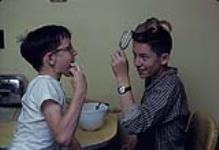 Alan Patrick, age 14, and his brother Brian Patrick, age 10, clean the icing after their mother bakes a cake - they are helped by Alan's pet chipmunk - Ottawa [between 1955-1963]