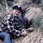 Charles Morency tenant un canard sur une colline couverte d'herbe, Île aux Basques, Québec [entre 1955-1963]