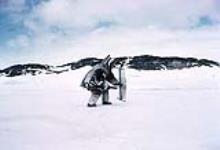 [Inuk man in caribou skin clothing holding a rifle and a taluutaaq] May 1959