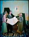 Tourists examine hand-loomed fabrics in handicrafts display of the New Brunswick School of Arts and Crafts, Fundy National Park. At center is instructor Archie Harper. juillet 1950.